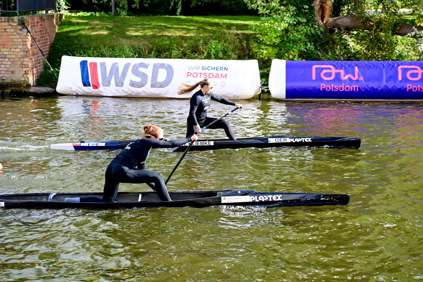 Zwei Canadier-Fahrerinnen Bord an Bord vor der WSD-Bande beim Potsdamer Kanusprint