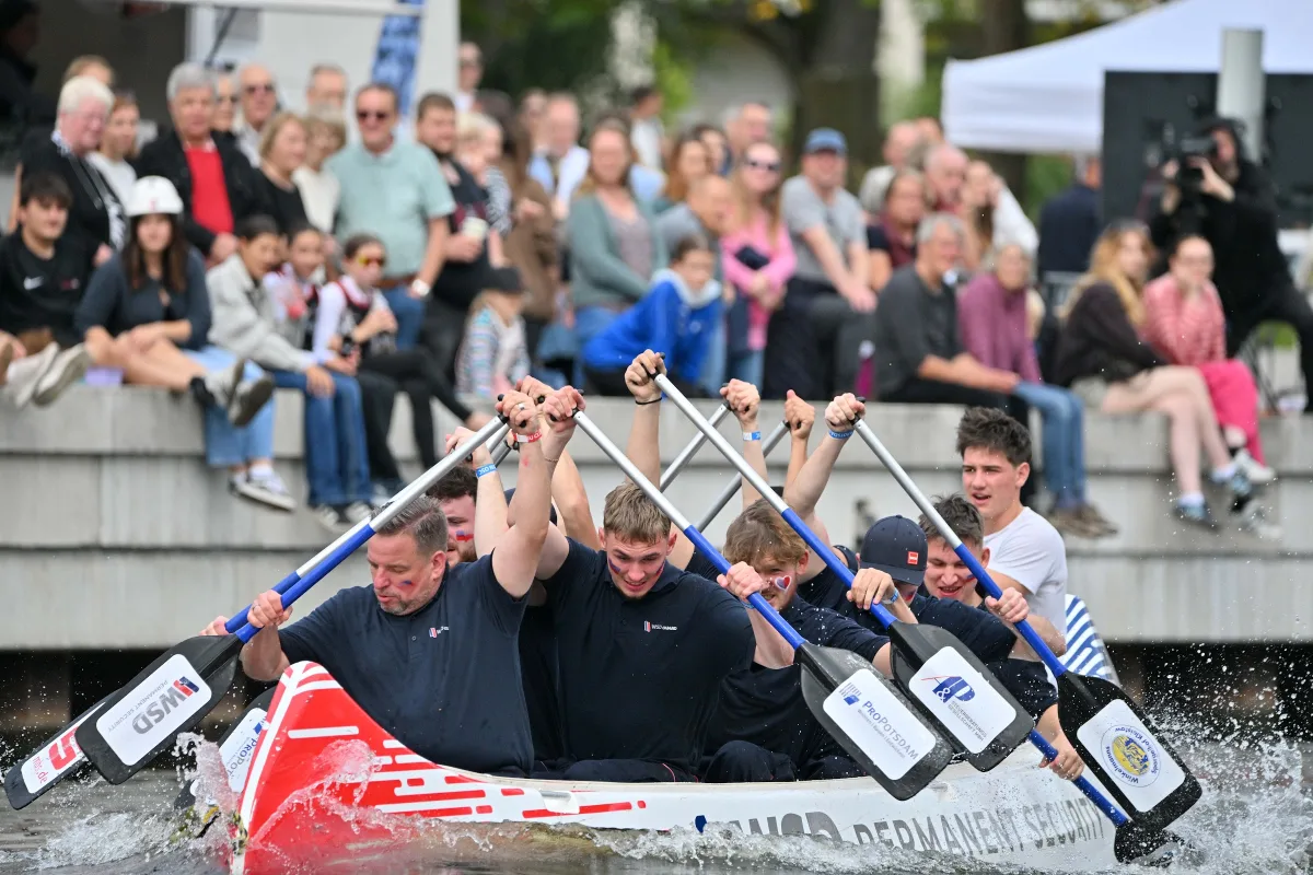 Drachenboot mit Besatzung vor dem Publikum auf den Uferstufen